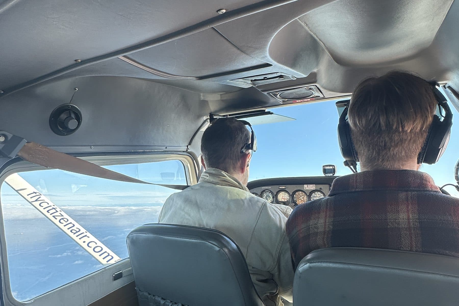 A pilot and an instructor in the front seats of a Citizen Air Cessna in flight, seen from the back seat