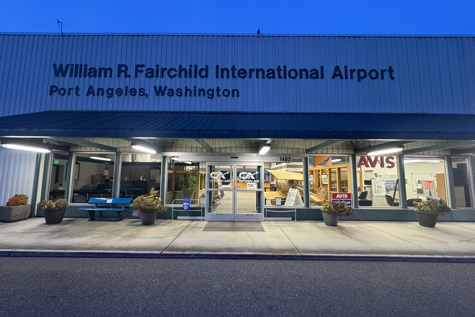The airport terminal at dusk, the Citizen Air and Avis signs lit